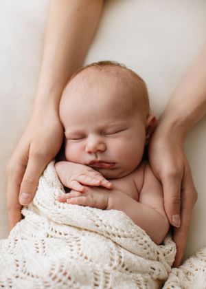 Sleeping newborn wrapped in knit blanket with gentle hands supporting.