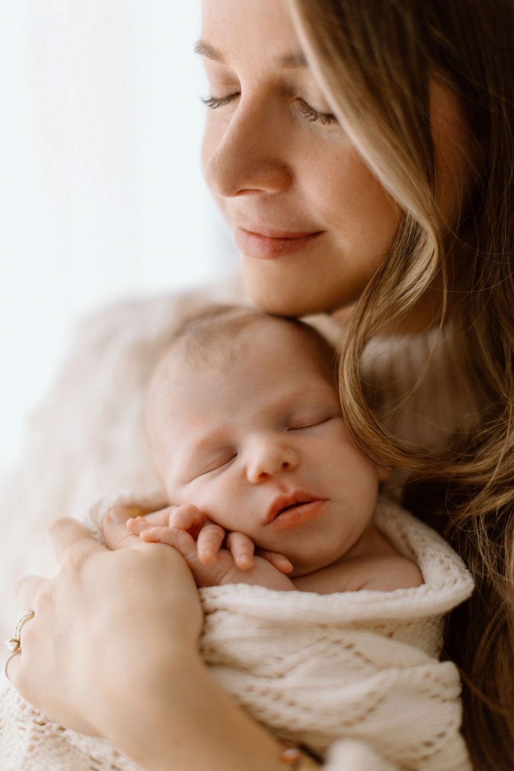 A tender moment captured in soft natural light as parent and baby share a gentle embrace.