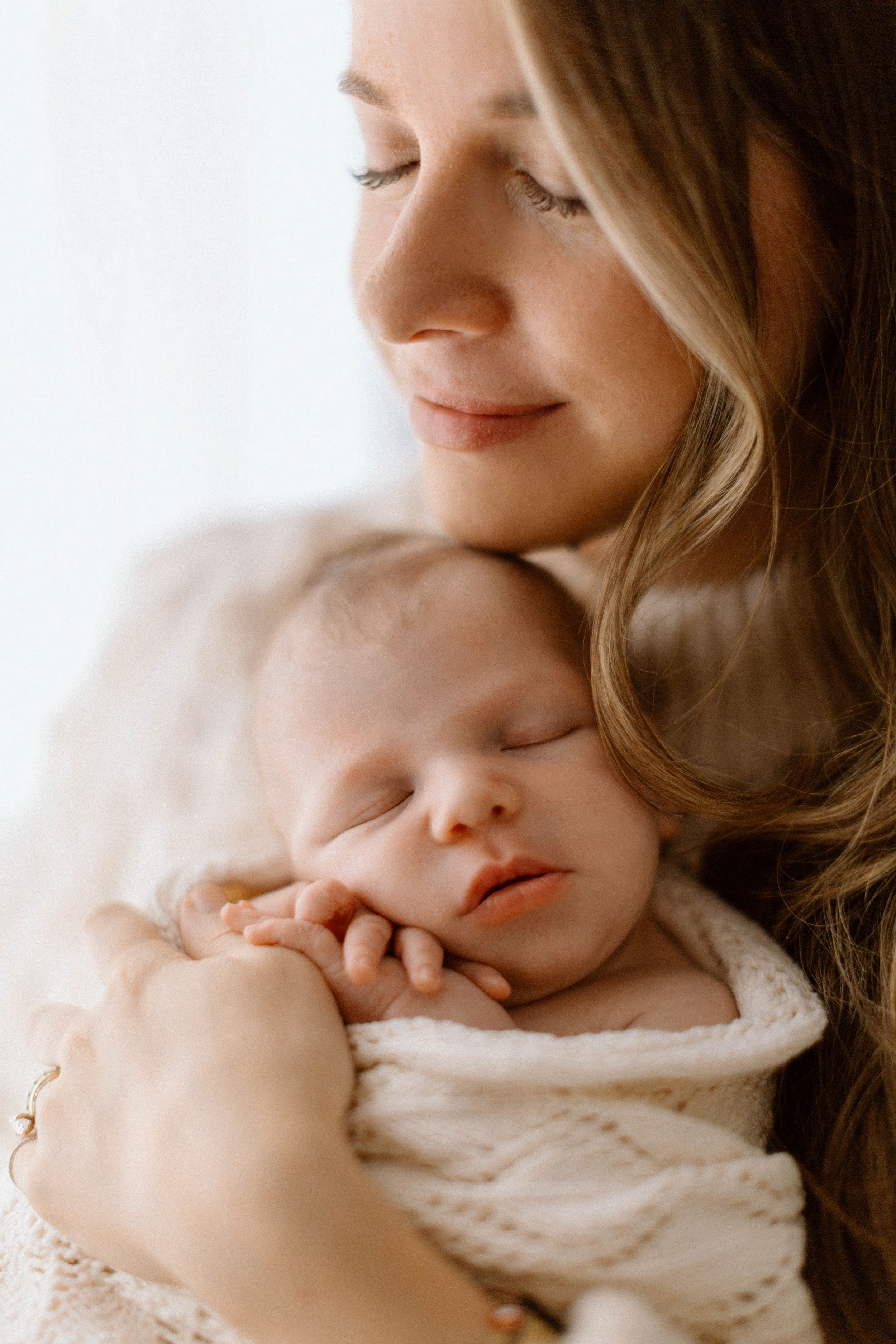 A tender moment captured in soft natural light as parent and baby share a gentle embrace.