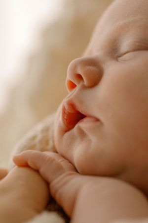 Close-up of a sleeping baby's face in warm lighting with tiny fist tucked under chin.