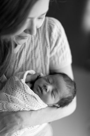 A tender black and white portrait of a sleeping newborn baby wrapped in delicate lace being cradled.