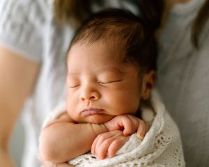 Peaceful sleeping newborn baby wrapped in soft white blanket with hand tucked under chin.