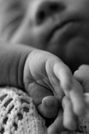 Close-up black and white photo of a tiny baby hand resting on soft knitted fabric with delicate skin details visible.