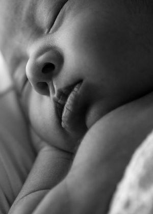 Close-up black and white photograph of a sleeping baby's face in soft focus with peaceful expression.