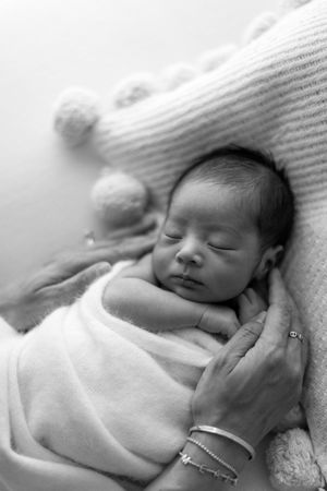 A peaceful sleeping newborn baby swaddled in white blankets rests against a soft textured backdrop.