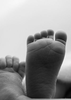 Close-up black and white photograph of tiny baby feet with delicate wrinkles and soft skin.