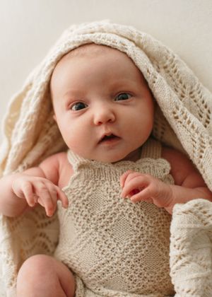 Baby wearing cream knitted romper swaddled in soft cream blanket during newborn photo session.