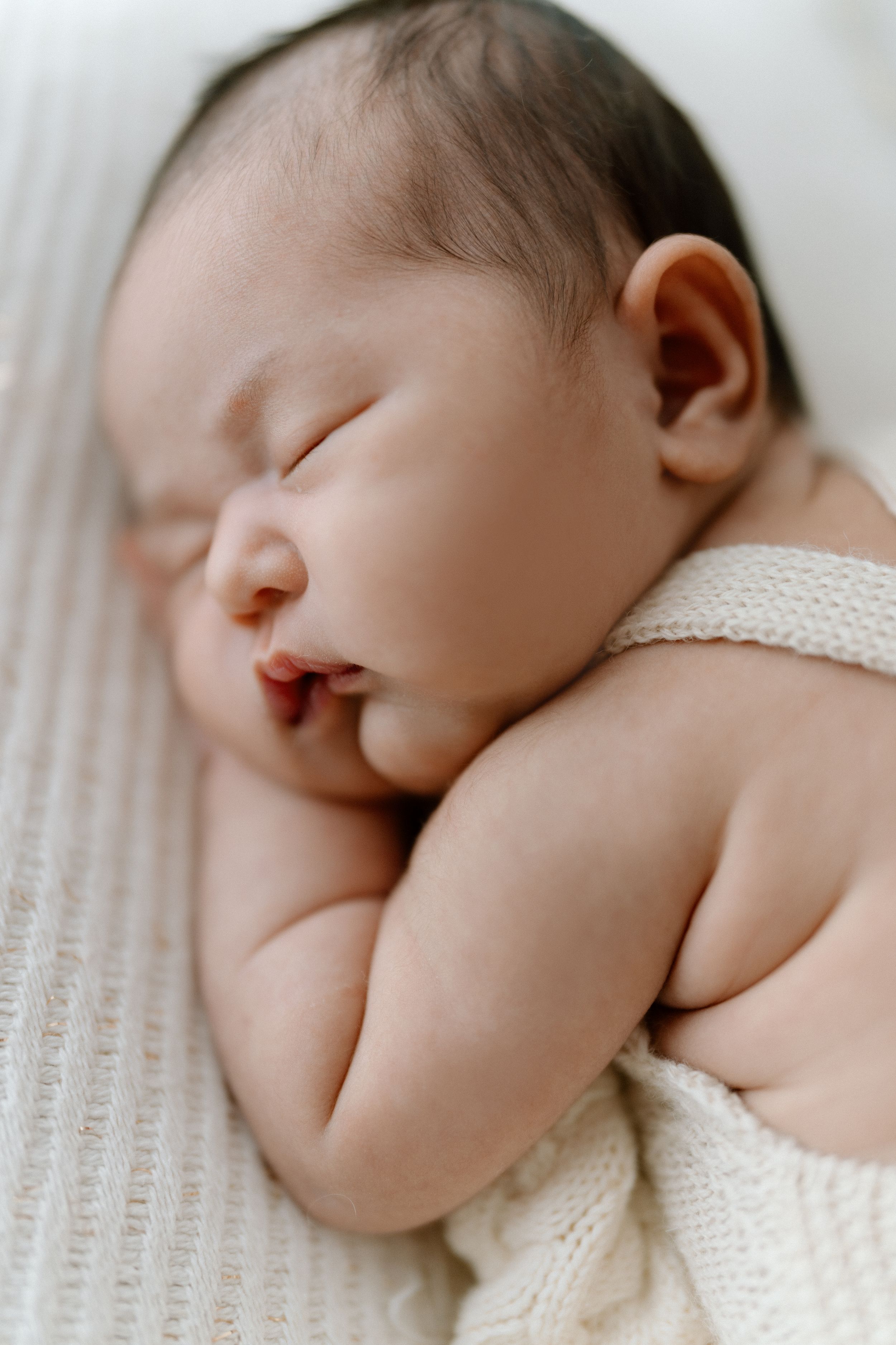 A series of five close-up photos showing a sleeping newborn baby in a white knit sweater against a light background.