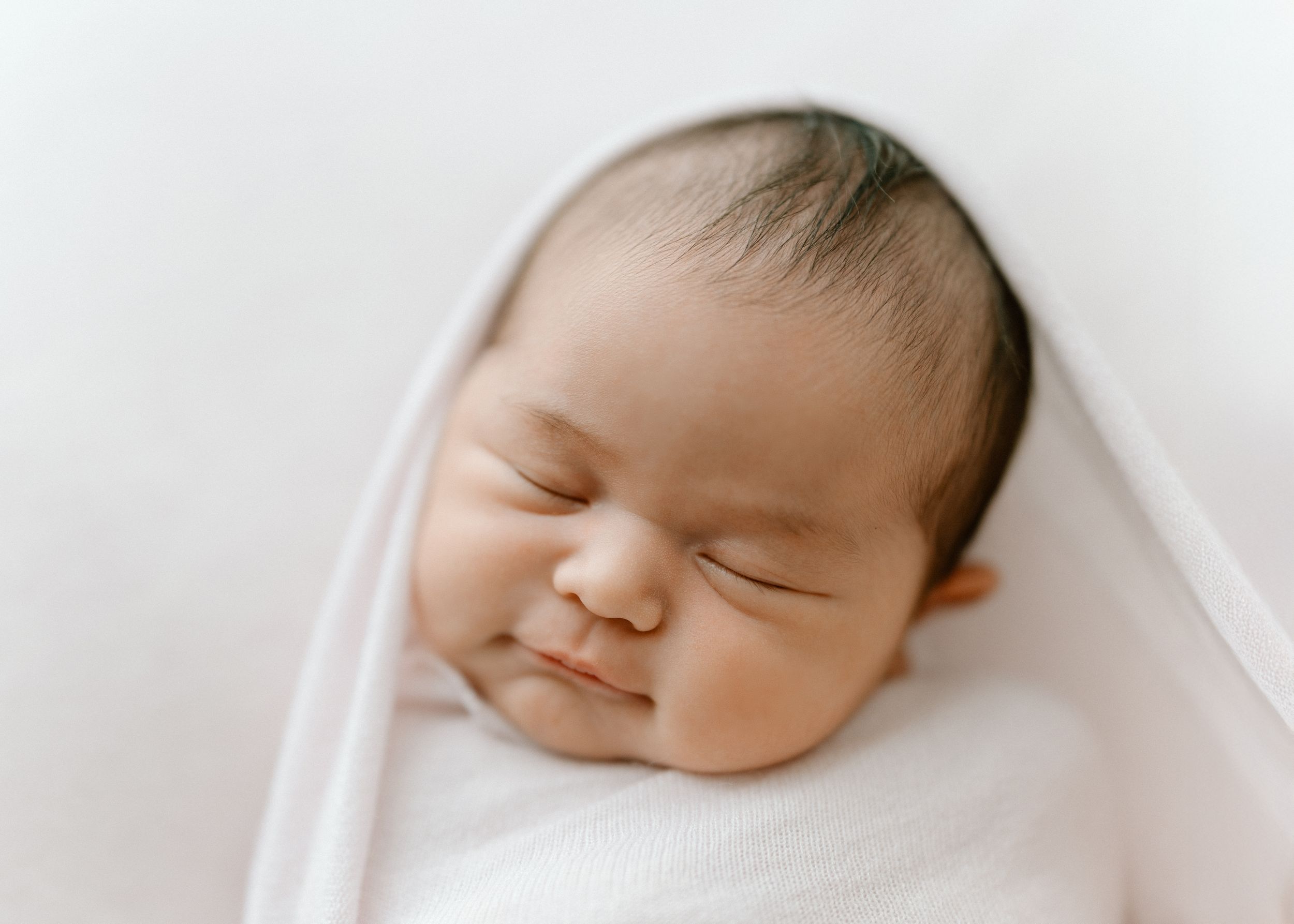 Peaceful sleeping newborn baby wrapped in soft white blanket in minimalist style photography.