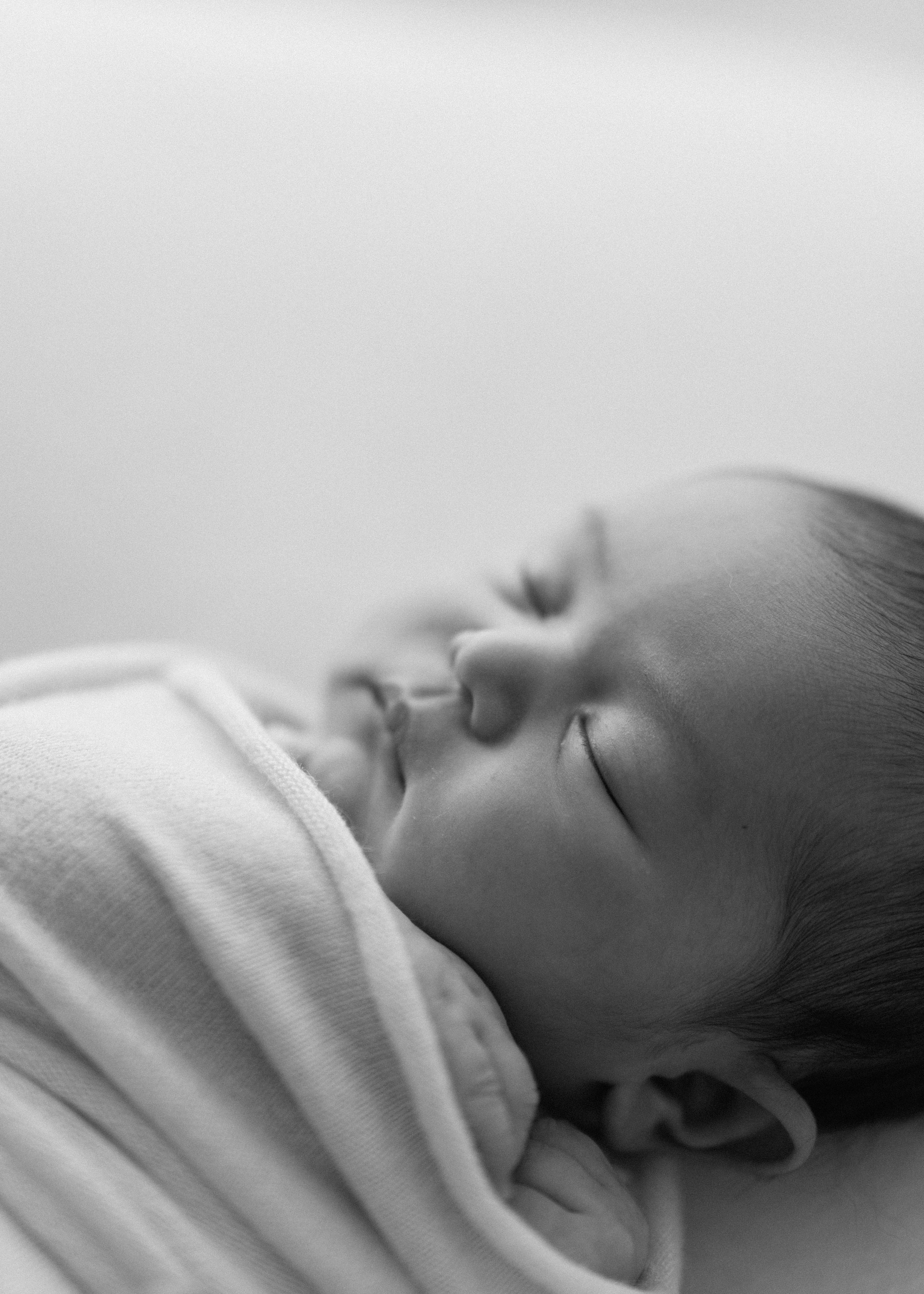 A peaceful black and white portrait of a sleeping baby swaddled in soft white fabric.