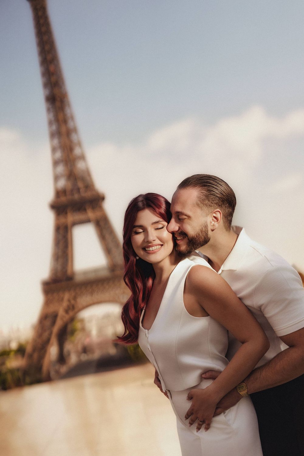 A romantic couple embraces near the iconic Eiffel Tower in Paris during a sunset photoshoot.