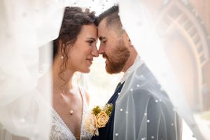 A tender wedding moment captured as couple touches foreheads under bridal veil.