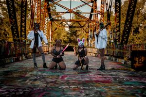 Four people pose creatively on a graffiti-covered bridge at sunset.