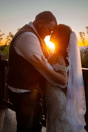 Silhouette of a couple in wedding attire embracing at sunset with golden sunlight glowing between them.