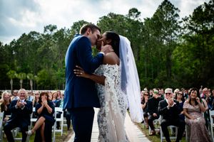 A romantic outdoor wedding ceremony with guests watching a couple share their first kiss under tall pine trees.