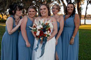 Wedding party in dusty blue bridesmaid dresses poses together outdoors at sunset.