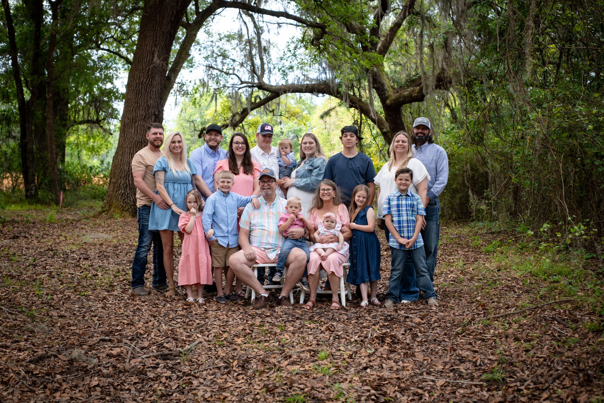 A large extended family gathering poses for a group photo in a wooded outdoor setting.