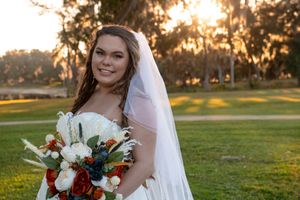A bride poses in a white wedding dress at sunset in a grassy field with warm golden lighting.