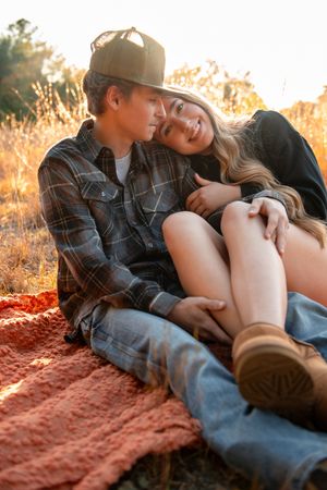 A couple relaxes together on a red blanket during golden hour sunset in a romantic outdoor setting.