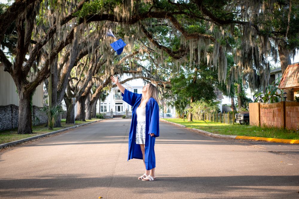 A graduation photo taken on a tree-lined street with Spanish moss hanging overhead.