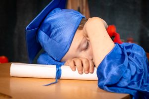 Graduate in blue cap and gown sleeping on diploma during graduation photo shoot.