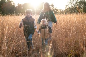 A group walks through tall golden grass during sunset in a field.
