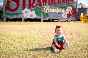 A vintage strawberry farm sign stands in a grassy field on a sunny day.