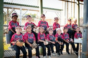 Youth softball team in pink uniforms poses for group photo on dugout bench.