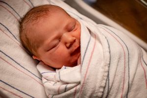 Sleeping newborn wrapped snugly in striped swaddle blanket.