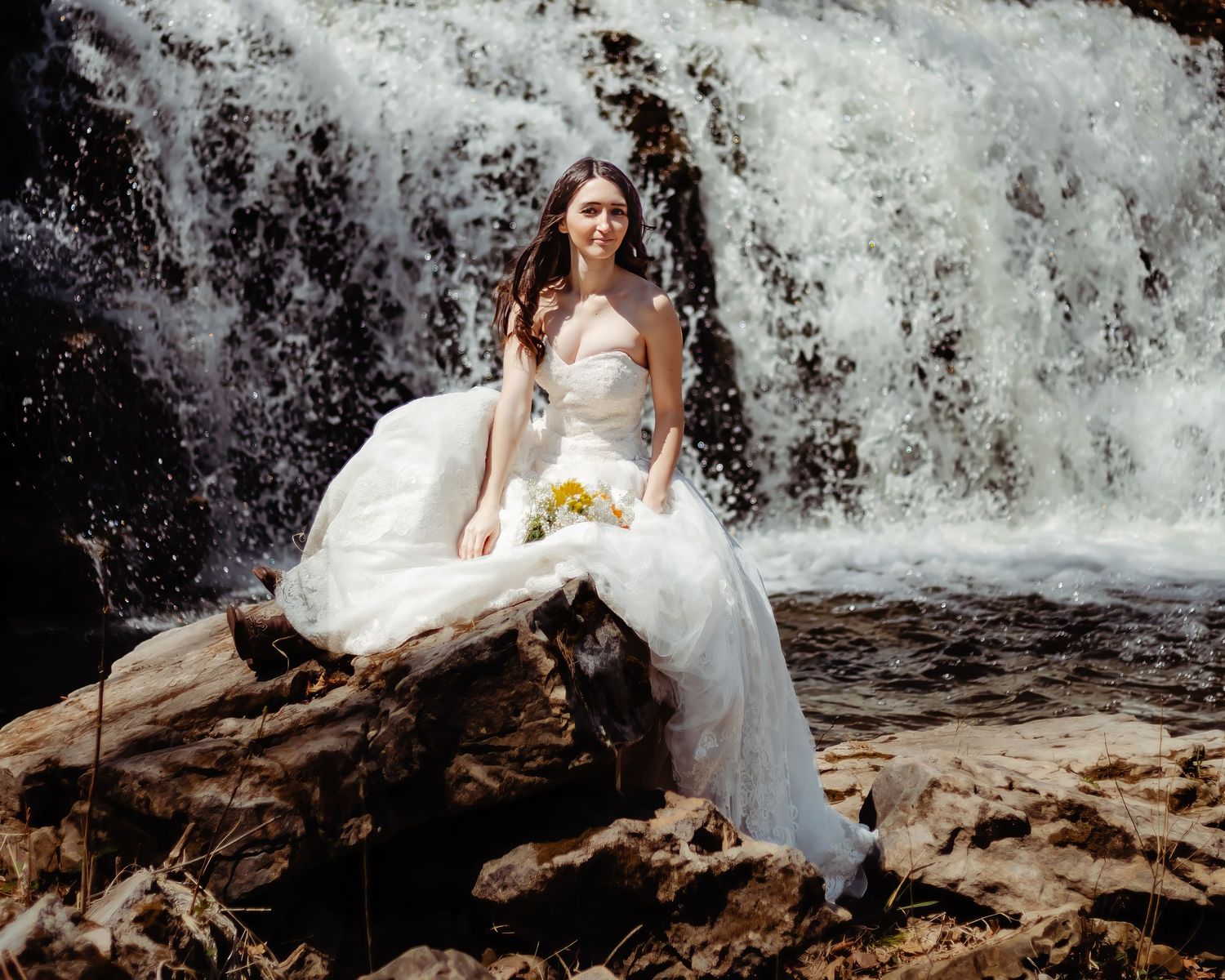 Elegant white wedding dress photographed against dramatic waterfall backdrop.
