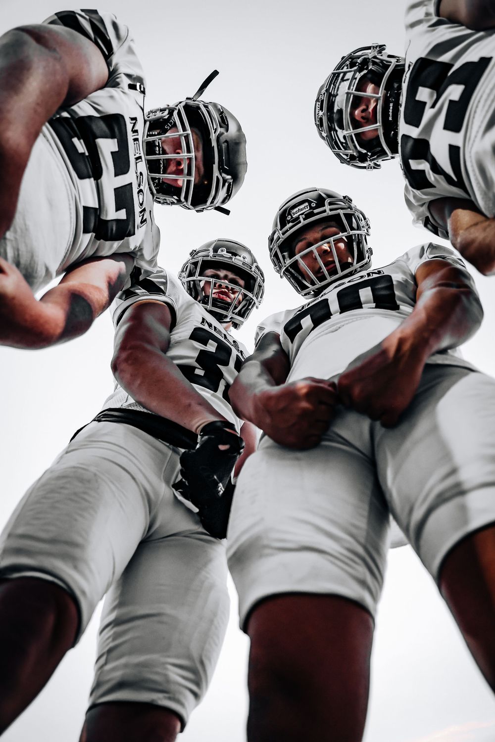 Low angle view of football players huddle in white uniforms against bright sky.