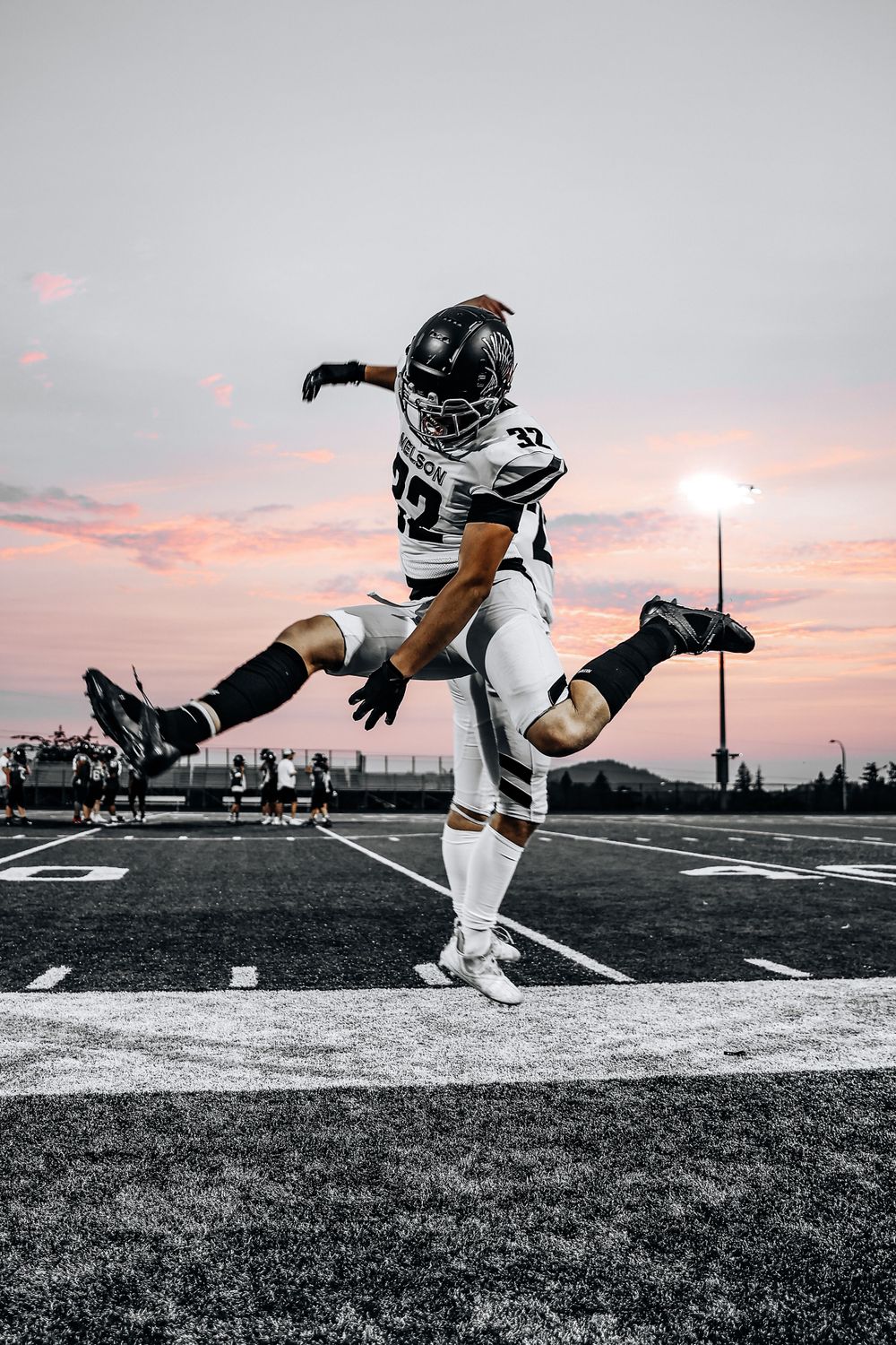 Football player in white uniform leaps gracefully against sunset sky on field.
