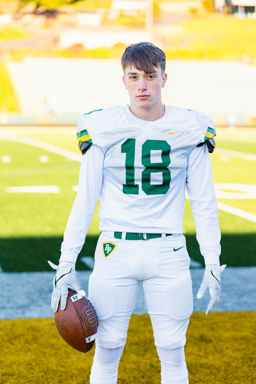 Football player in white uniform number 18 poses with ball on sunny field.