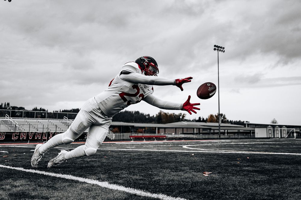 Football player diving to catch ball in dramatic black and white photo.