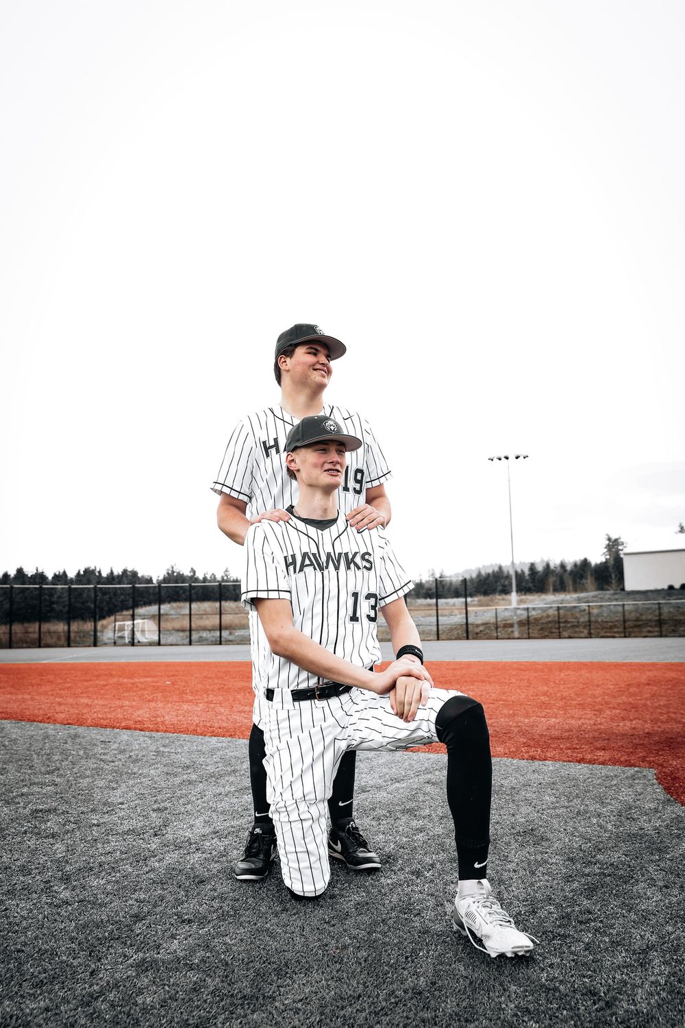Two baseball players in pinstriped Hawks uniforms pose on the field for a team photo at their sports facility.