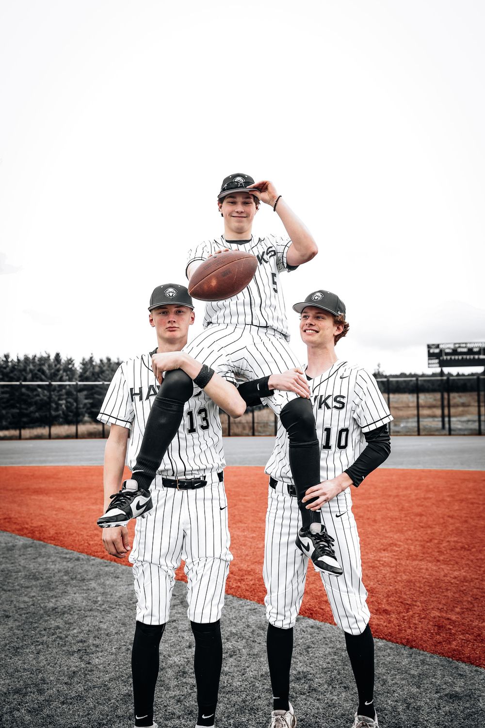 Youth baseball players in pinstripe uniforms joke around and show team spirit during practice on a red clay field.