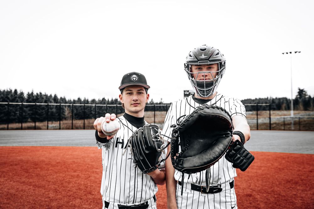 Two baseball players in striped uniforms stand on dirt field with pitcher showing grip and catcher holding mitt.