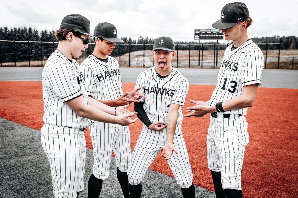 Baseball players in pinstriped uniforms gather on a red dirt field sharing a lighthearted moment during practice.