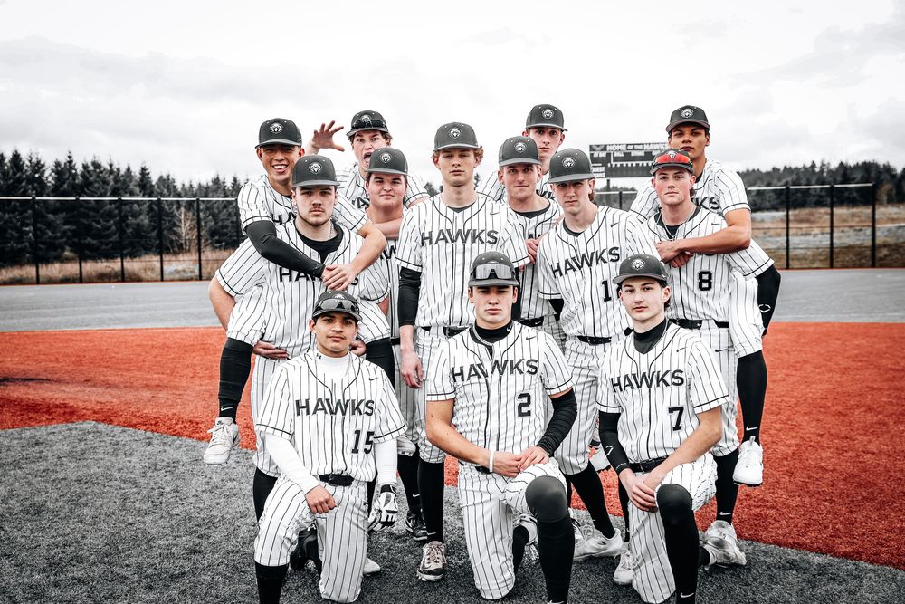Baseball team in pinstriped uniforms poses together on red clay field with pine trees in background.