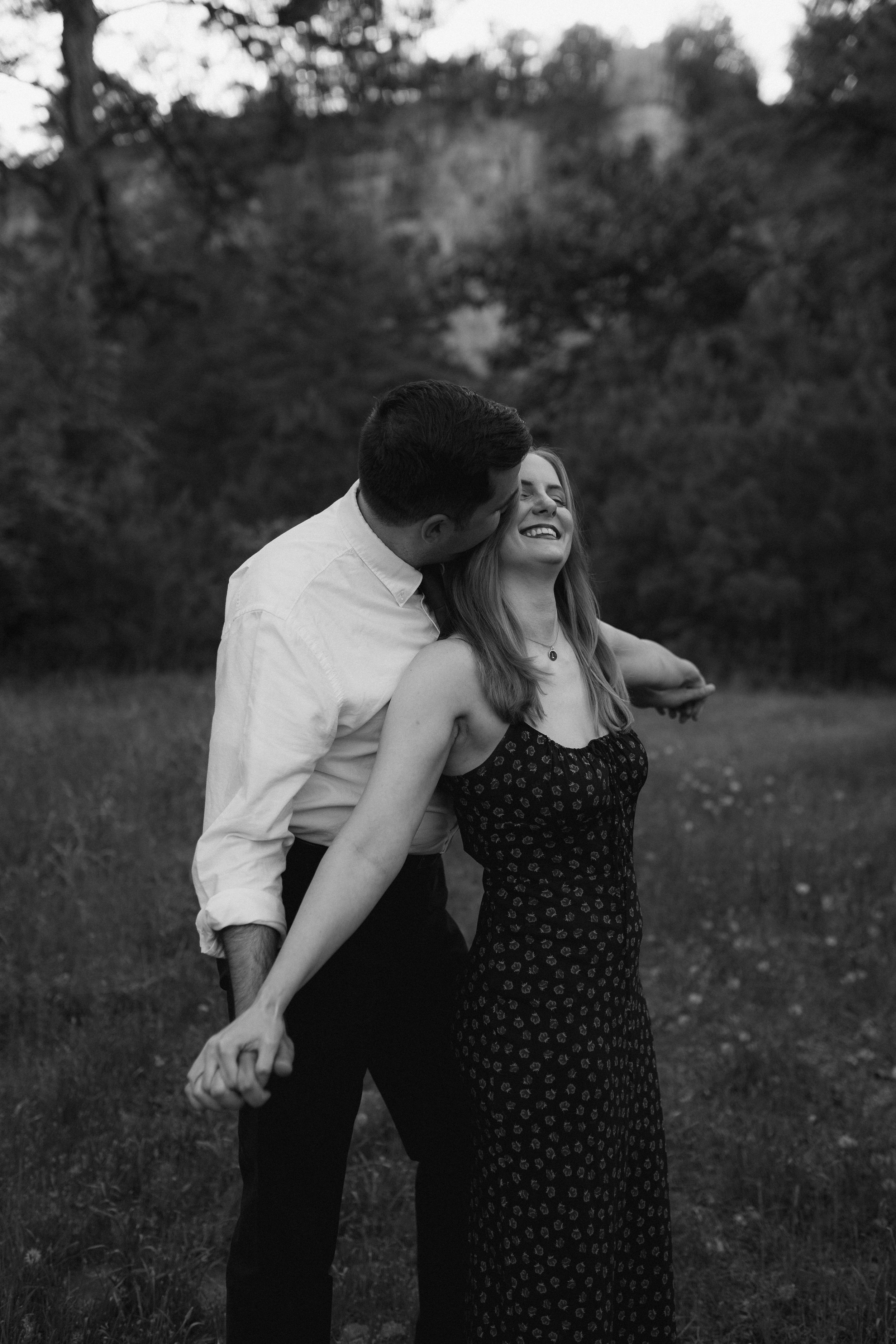 Black and white romantic outdoor engagement photo shoot of couple laughing together in a field.