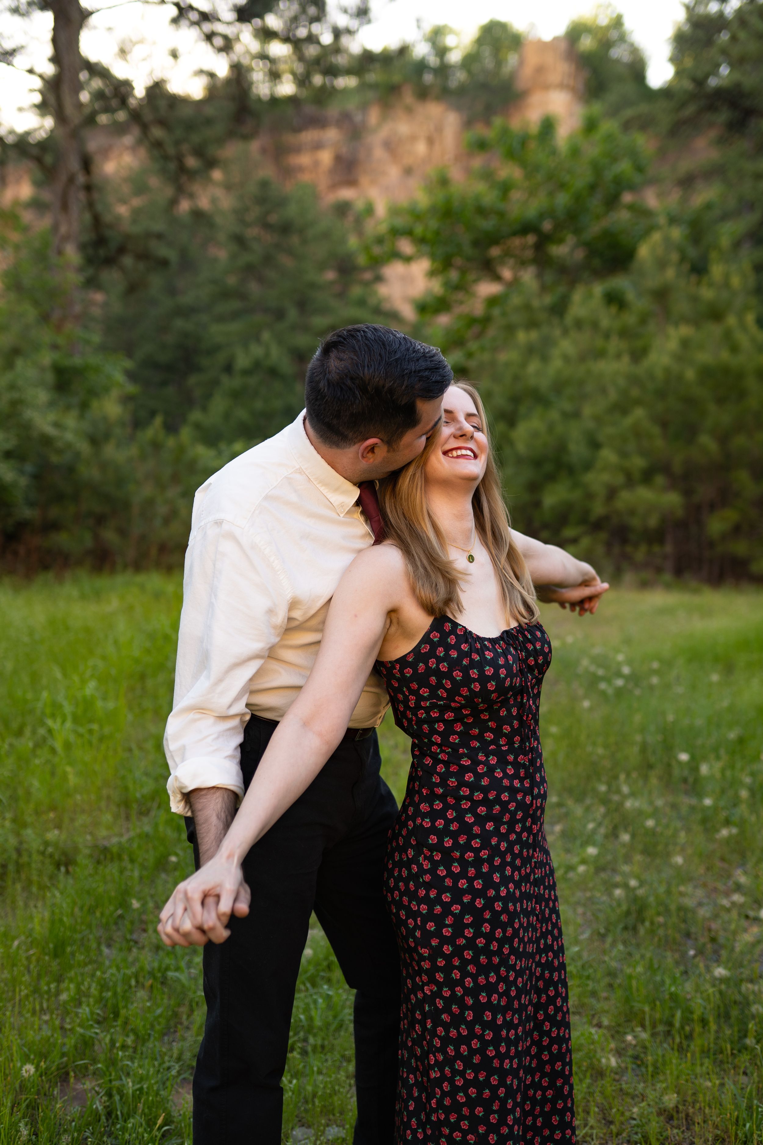 Couple shares playful laughter while sitting in natural outdoor setting at sunset.