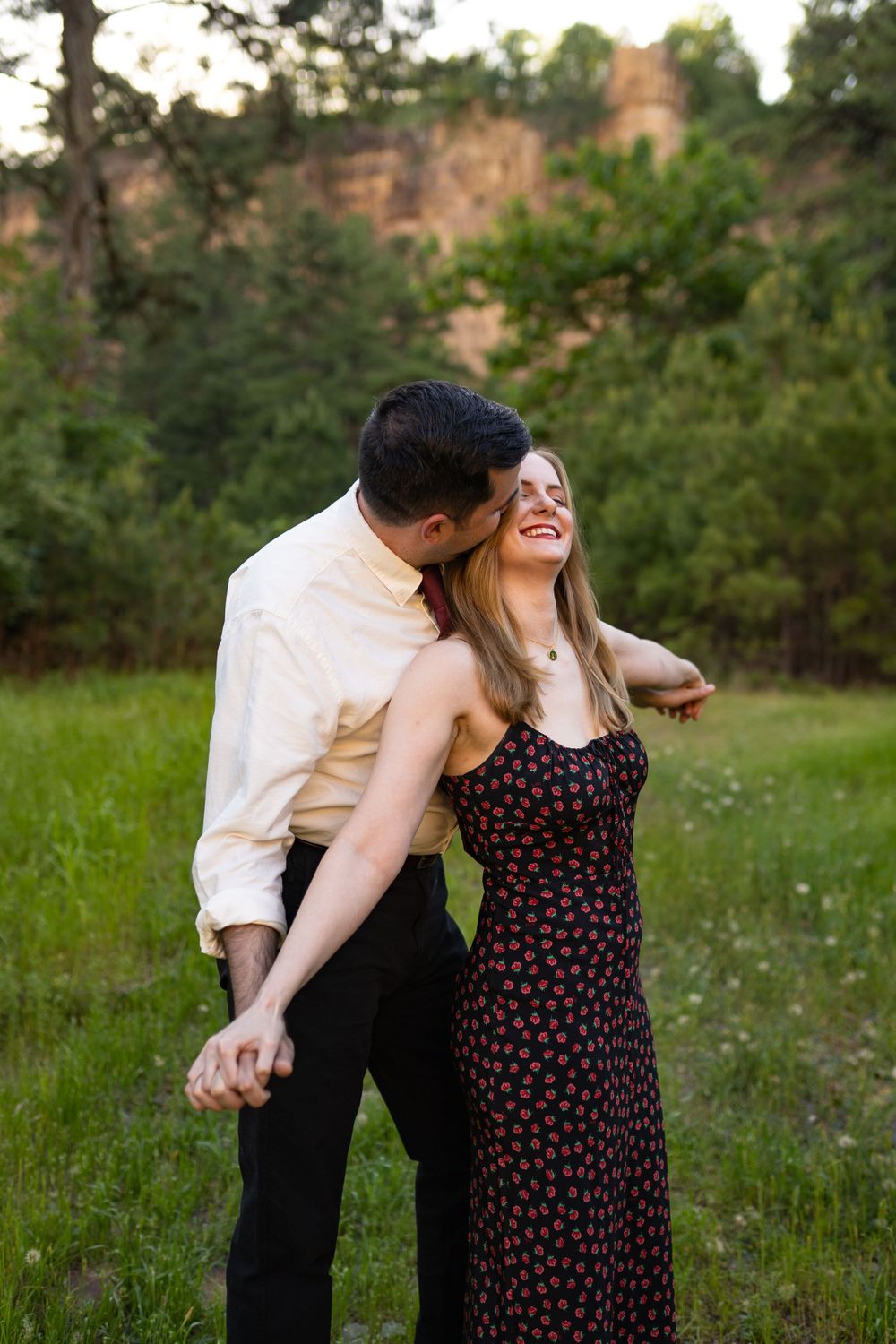 Couple shares playful laughter while sitting in natural outdoor setting at sunset.