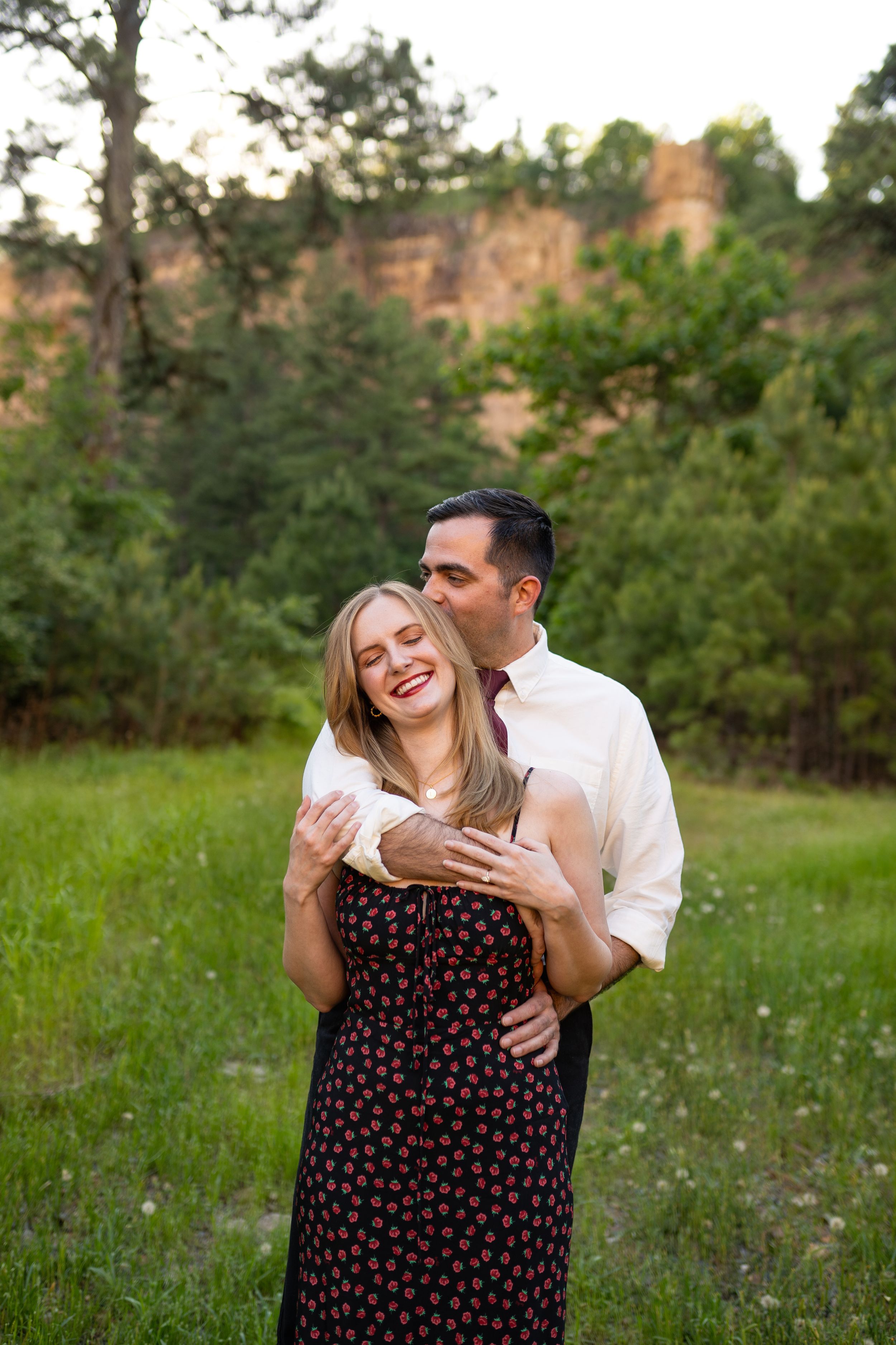Happy couple embraces and laughs together in meadow with mountain backdrop.