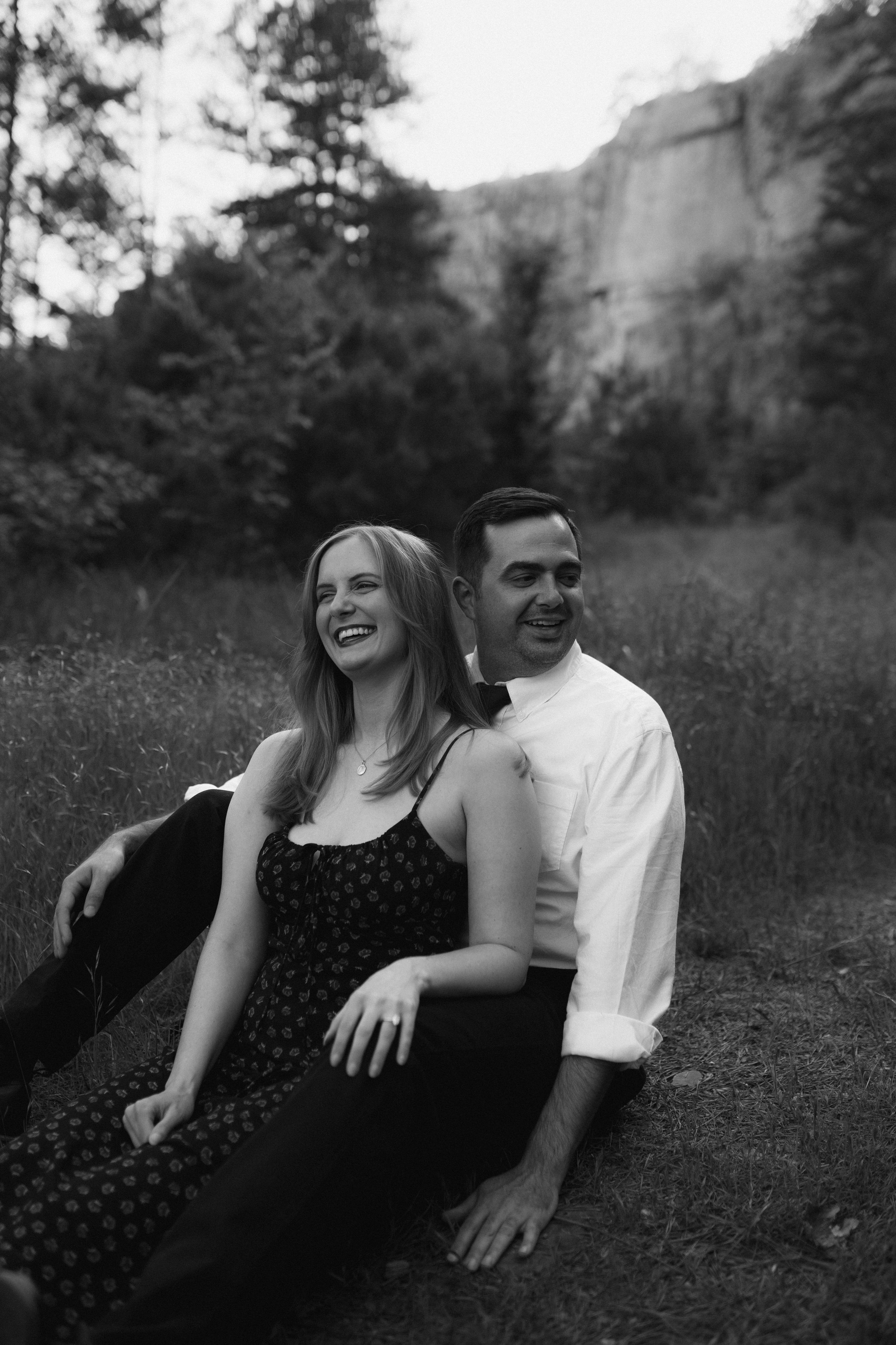 Playful couple shares joyful moment together during outdoor photo session in field with trees.