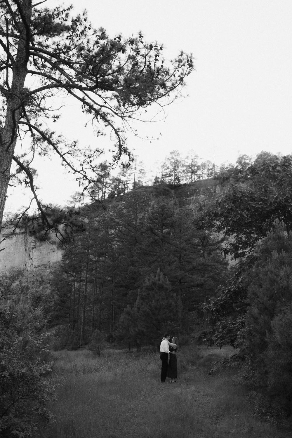Black and white landscape photo of distant figures in wooded hillside setting.