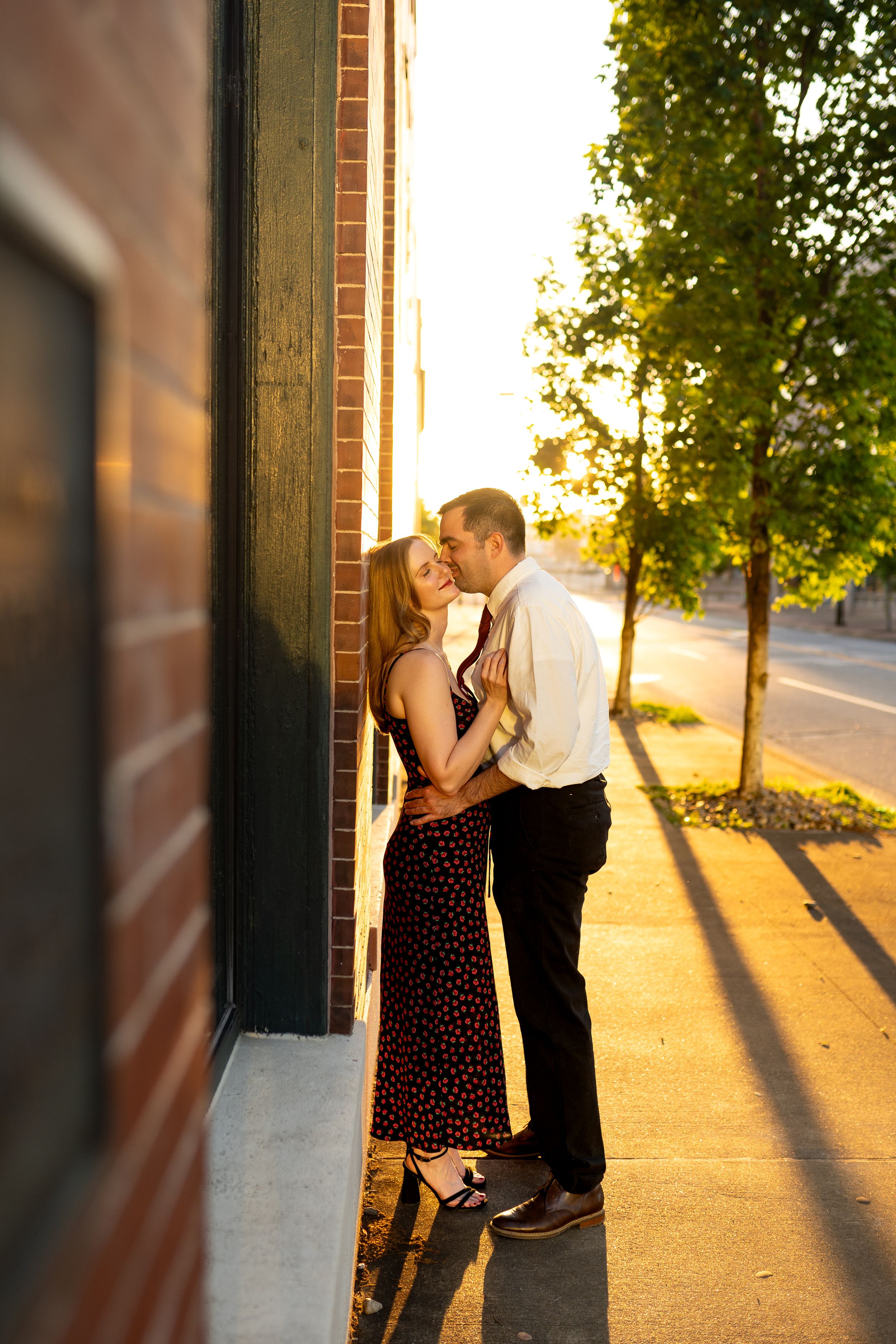 Romantic sunset moment between couple against brick building with dramatic lighting.