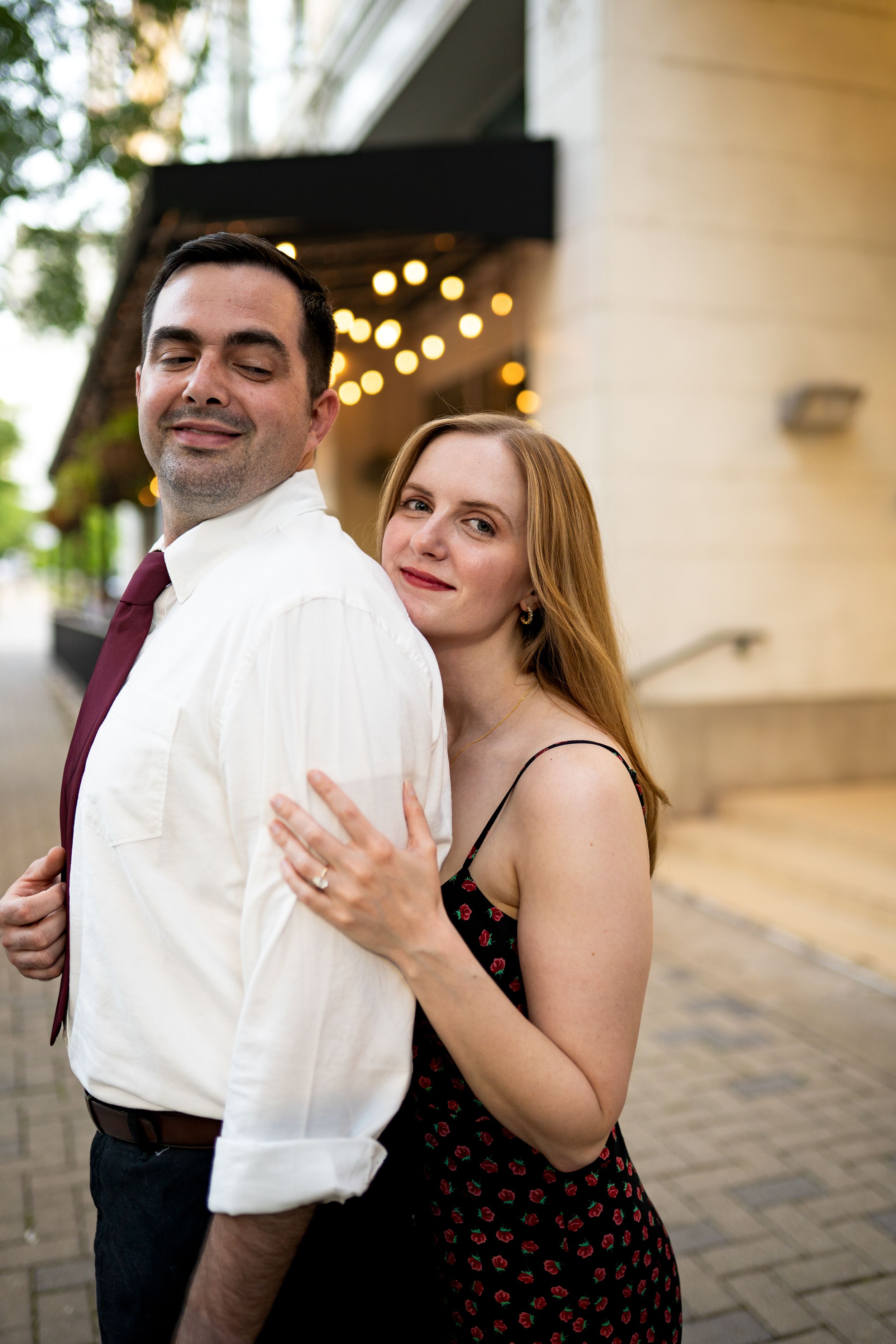 Couple embraces by column with string lights creating romantic ambiance.