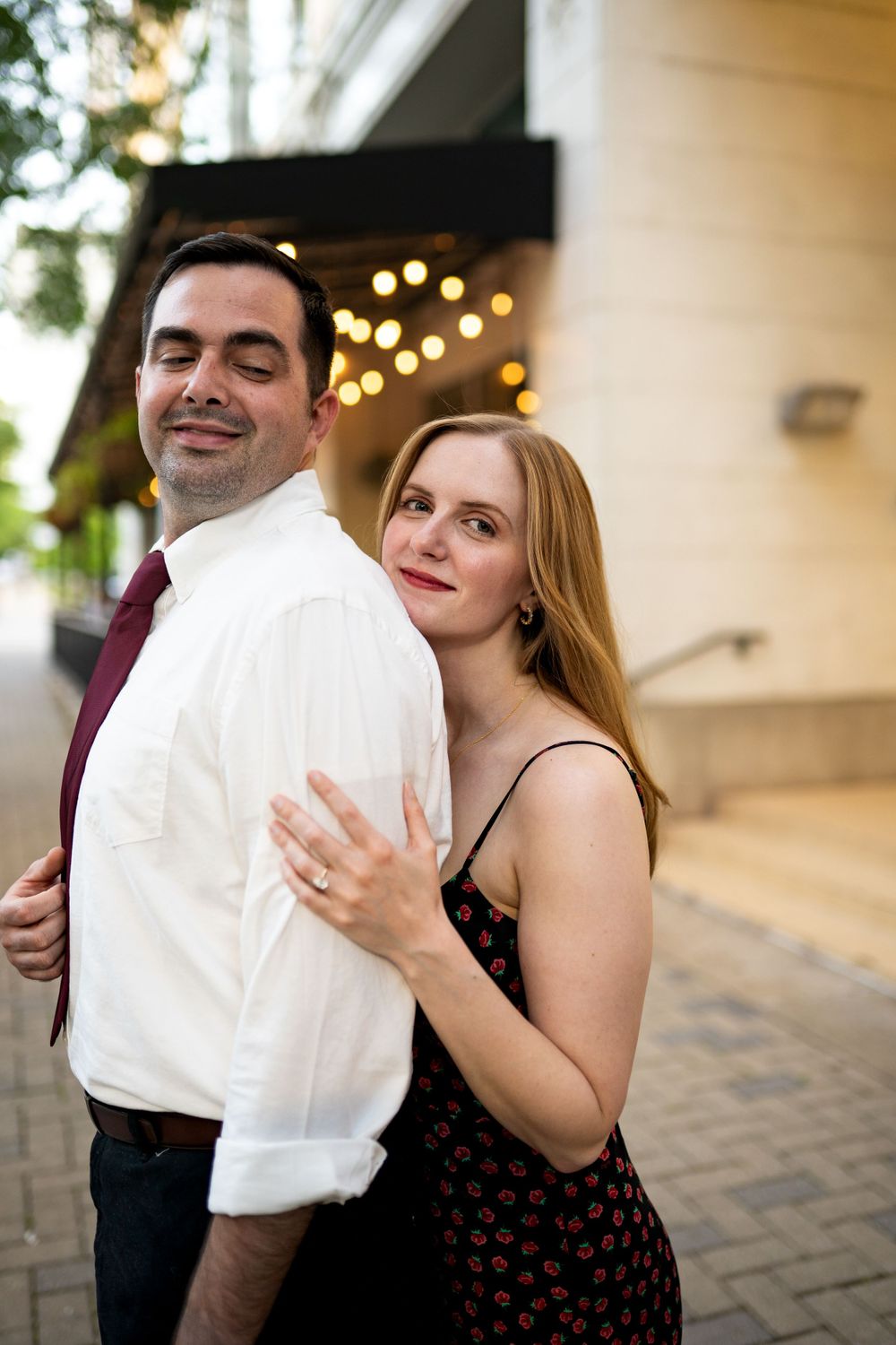Couple embraces by column with string lights creating romantic ambiance.