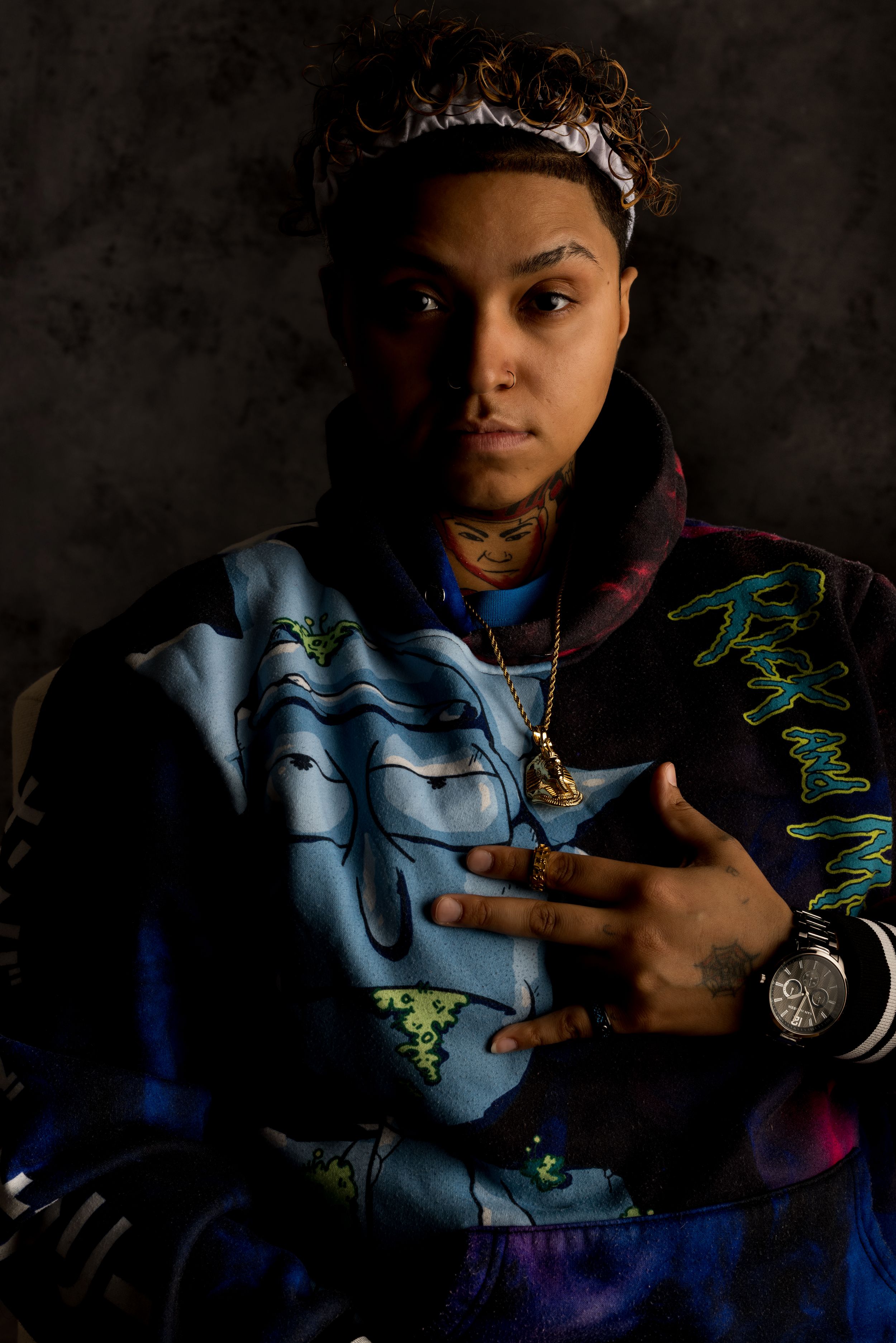 Dramatic portrait with moody lighting features a person wearing a vibrant jacket decorated with graffiti-style artwork.