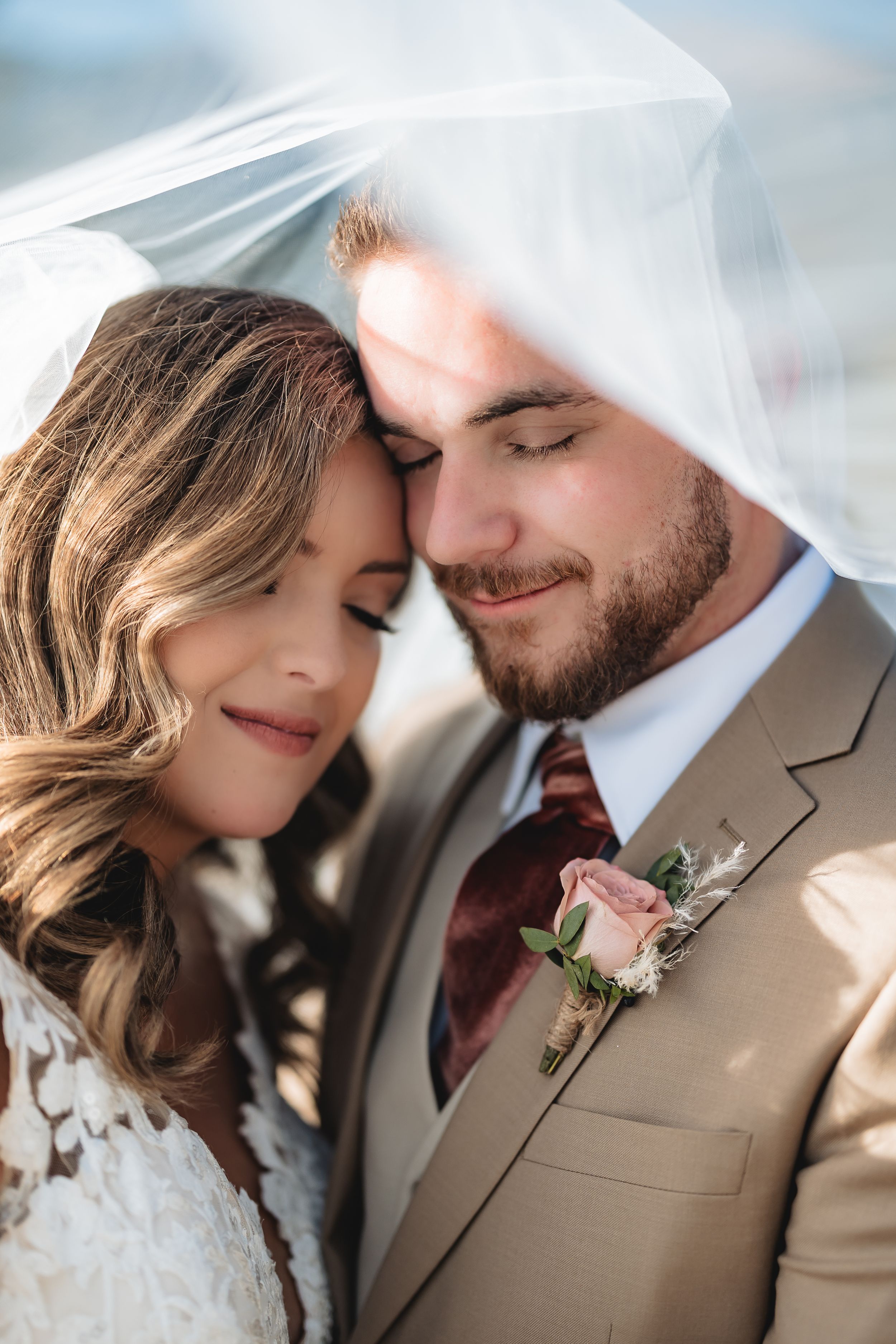 A romantic wedding portrait shows a tender moment under a flowing white veil.